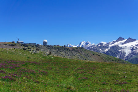 panoramic mountain landscape with alpine meadow, observatory in the distance and mountain peaks in the backgroundの写真素材