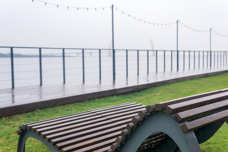 bench in a public space on the embankment on the shore of a foggy bay with a bridge in the distance on a rainy dayの写真素材