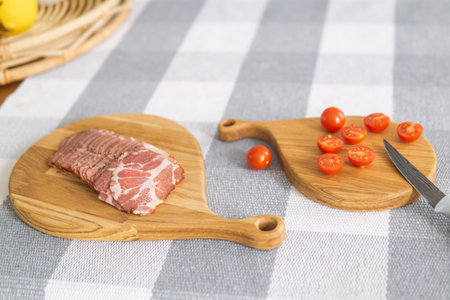 cherry tomatoes and sliced ham on a cutting boards on a tableの写真素材