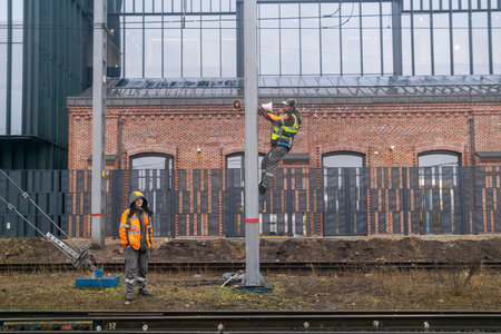 Perm, Russia - November 10, 2025: workers install a warning system on a pole on a railway against a backdrop of industrial buildings.のeditorial素材