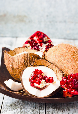 Fresh coconut and red garnet in a wooden bowl,blue background, tropical fruitの写真素材