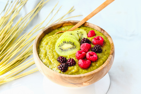 Green smoothies with spirulina bowl, pears, kiwis and berries, raw breakfast, wooden tableware,light backgroundの写真素材