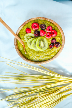 Green smoothies with spirulina bowl, pears, kiwis and berries, raw breakfast, wooden tableware,light backgroundの写真素材