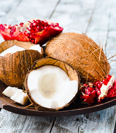 Fresh coconut and red garnet in a wooden bowl,blue background, tropical fruitの写真素材
