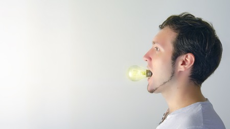 Multi-ethnic man with a short beard and a light bulb in his mouth. I have an idea on a gradient white-gray background.の写真素材