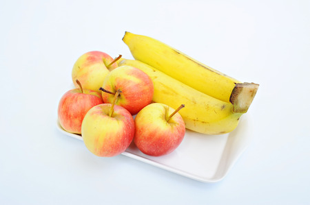 Ripe bananas and apple in dish on white backgroundの写真素材