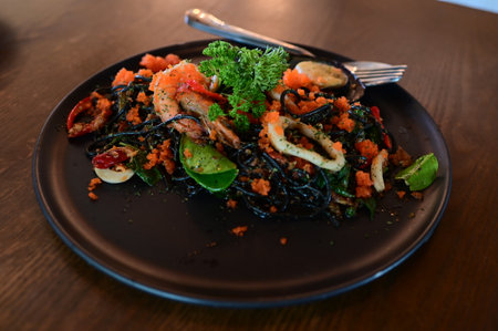 Seafood pasta on a black plate on a wooden table.の写真素材