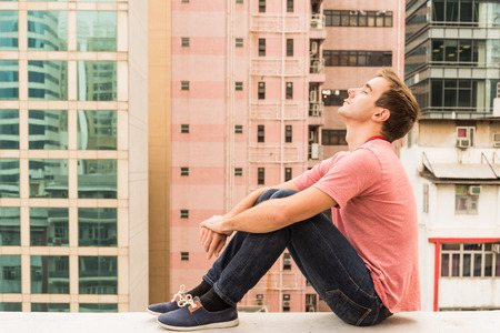 Man sitting on a Corbel on a Rooftop of Hong Kong Islandの写真素材