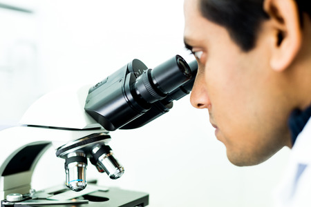 A concentrated Researcher working with a Microscope in a Biochemistry Labの写真素材