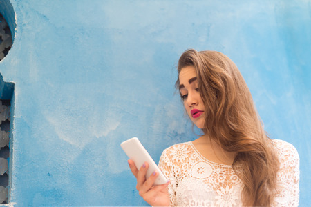 Pretty Girl reading news on her Phone on a blue Wallの写真素材