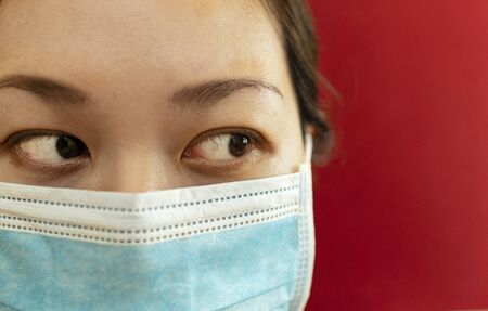 Coronavirus theme. Asian woman  wearing a mask to protect herself from getting infected on a red background.の写真素材