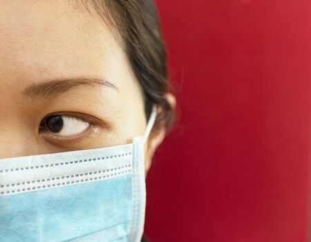 Coronavirus theme. Asian woman  wearing a mask to protect herself from getting infected on a red background.の写真素材