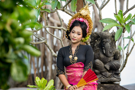 Bali asia woman in front of a statue of Ganesha wearing a red black suit costumeの写真素材