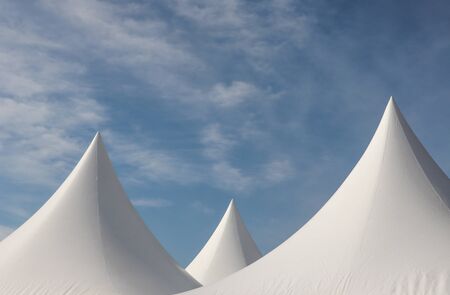 A row of white triangular pyramid marquee rooftops against a blue skyの写真素材
