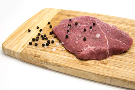 Raw beef steak from young bull with salt and pepper on cutting board on white isolated backgroundの写真素材