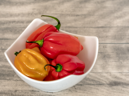 Habanero pepper, jalapeno, capsicum annuum, small spicy peppers in a white bowl, wood background.