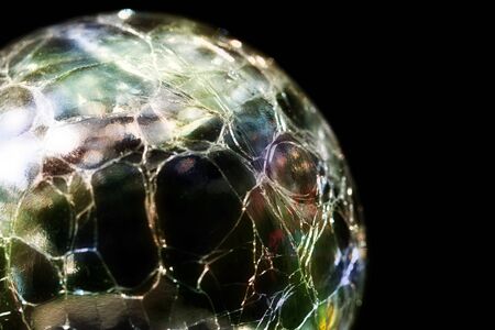 Glass ball with a splintered surface and colored reflections against a black backgroundの写真素材