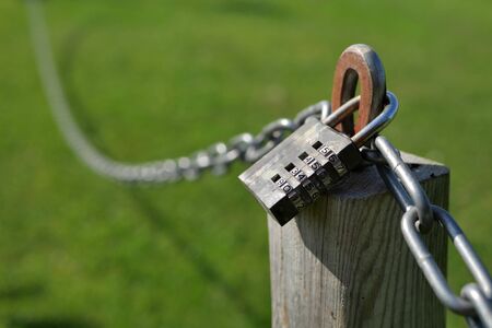 Combination lock secures a chain attached to a wooden post.の写真素材