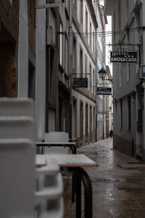 Santiago de Compostela, Galicia, Spain - 09/26/2020: Stacked plastic chairs and tables in a narrow empty hostel street with a closed cafe.のeditorial素材