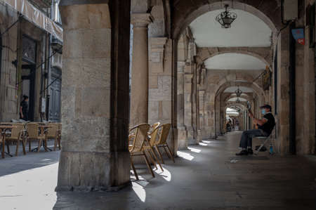 Santiago de Compostela, Galicia, Spain - 09/22/2020: Elderly Spanish man playing guitar under stone archways in the street wearing a medical mask.のeditorial素材