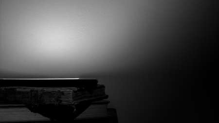 A small stack of old books with an electronic e-reader positioned on top illustrating technological change. Black & white background with dramatic lighting.の写真素材