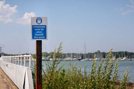 Life jacket warning sign by the sea with yachts in the background.