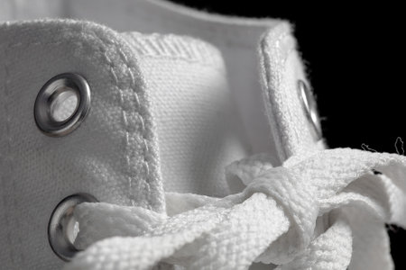 Closeup of a lighty used white trainer sneaker laces made of fabric on a black bckground. Footware fashion clothing sportの写真素材