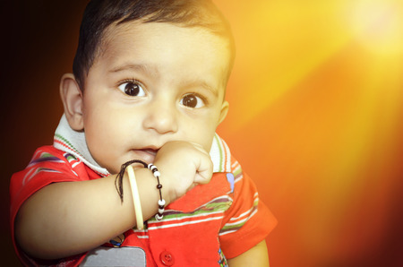 happy infant baby boy in red dress with hand in his mouthの写真素材