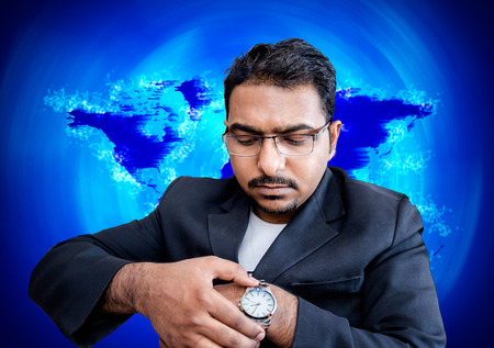 asian indian businessman with eye glasses fixing time on writ watch  on world map backgroundの写真素材