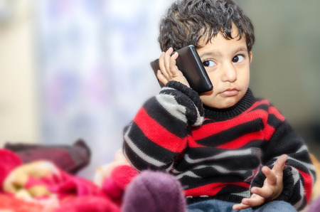 boy child talking over mobile phone sitting on bedの写真素材