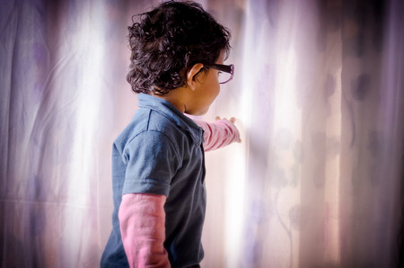 Portrait of asian Indian boy child looking behind curtain wearing eye glassの写真素材