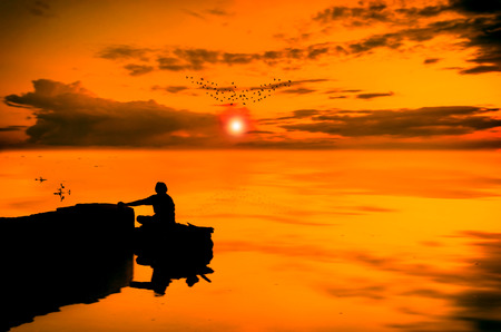 man silhouette sailing on boat in a dream like scene in the river or sea towards the sun in the dramatic sky where sun is shining through clouds at sunset or sunrise and birds silhouette flying home, composed in Adobe Photoshop cc 2014 using advance photoの写真素材