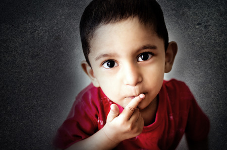 indian asian boy little child putting finger on mouth with small hairs looking straight into camera headshot shot with nikon d-5100 with 35mm 1.8 g prime lens post processed in adobe photoshop lightroom and photoshop ccの写真素材