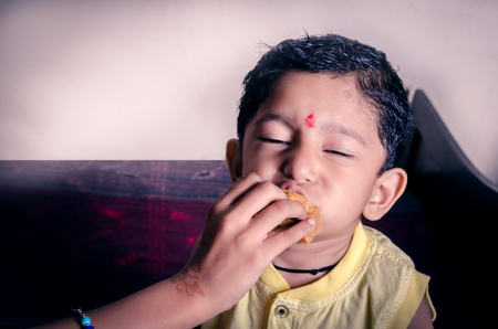 little indian asian boy child eating sweets with closed eyes enjoying the delicious flavourの写真素材