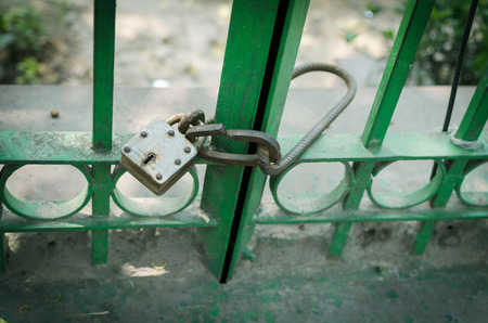 close up shot of lock with key in the keyhole locked on green iron rod outside park boundary wallの写真素材