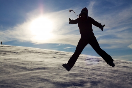 Silhouette of jumping girl on snow against the sun, concept of youth, energy, active lifeの写真素材
