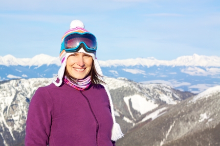Smiling attractive young woman wearing knitted winter cap and ski glasses with picturesque winter backgroundの写真素材