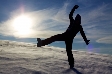 Silhouette of jumping girl on snow against the sun, concept of youth, energy, active lifeの写真素材