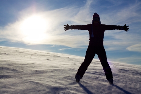 Silhouette of girl in snow spreading hands with sun in the backgroundの写真素材