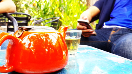 Close up of a red kettle on a table with a man playing his mobileの写真素材