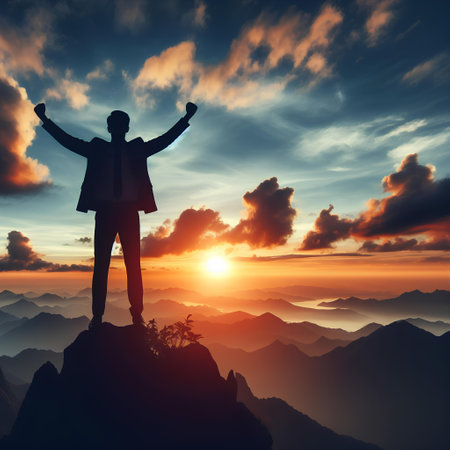 Silhouette of a successful businessman standing on the top of a mountain and raised his hands to the sky.の素材
