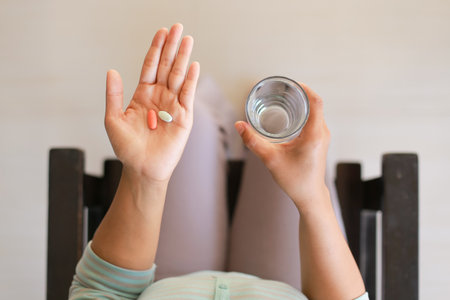 Closeup of woman hands with pills and glass of water at homeの写真素材