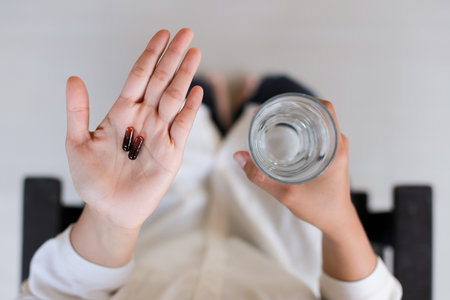 Close up of a woman holding a pill and a glass of waterの写真素材