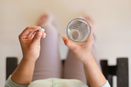 Close up of woman holding a pill and a glass of water at homeの写真素材