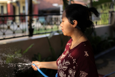 Woman Watering Plants Outdoors in Daylight Wearing Headphonesの写真素材