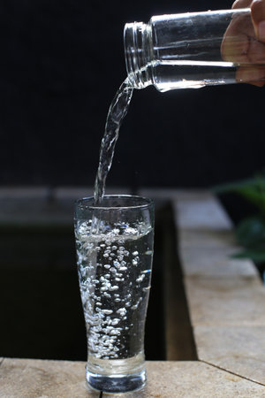 Pouring water into a glass on the wooden table with black background