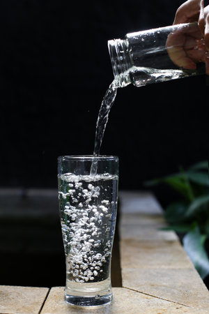 Pouring water into a glass on a wooden table with black backgroundの写真素材