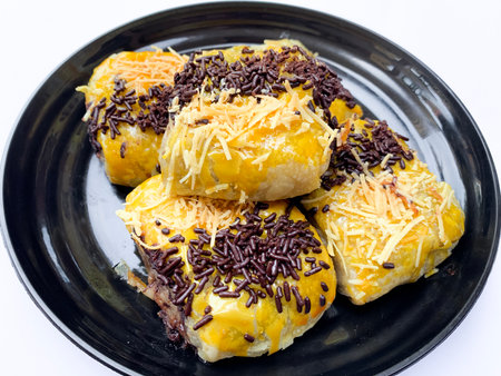 Close-up Indonesian chocolate banana bolen cake,indonesian banana puff pastry, garnished with grated cheese and chocolate. on a black plate isolated on white backgroundの写真素材
