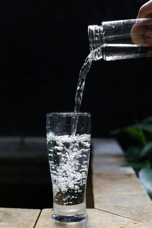 Pouring water into a glass on a wooden table. Black background.の写真素材