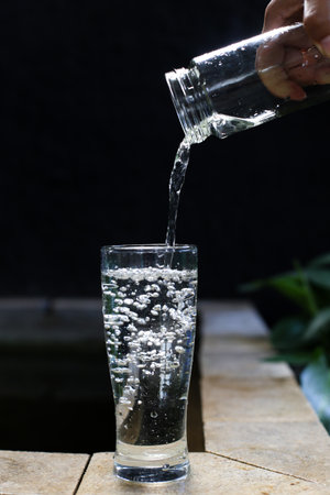Pouring water into a glass on a wooden table with black backgroundの写真素材